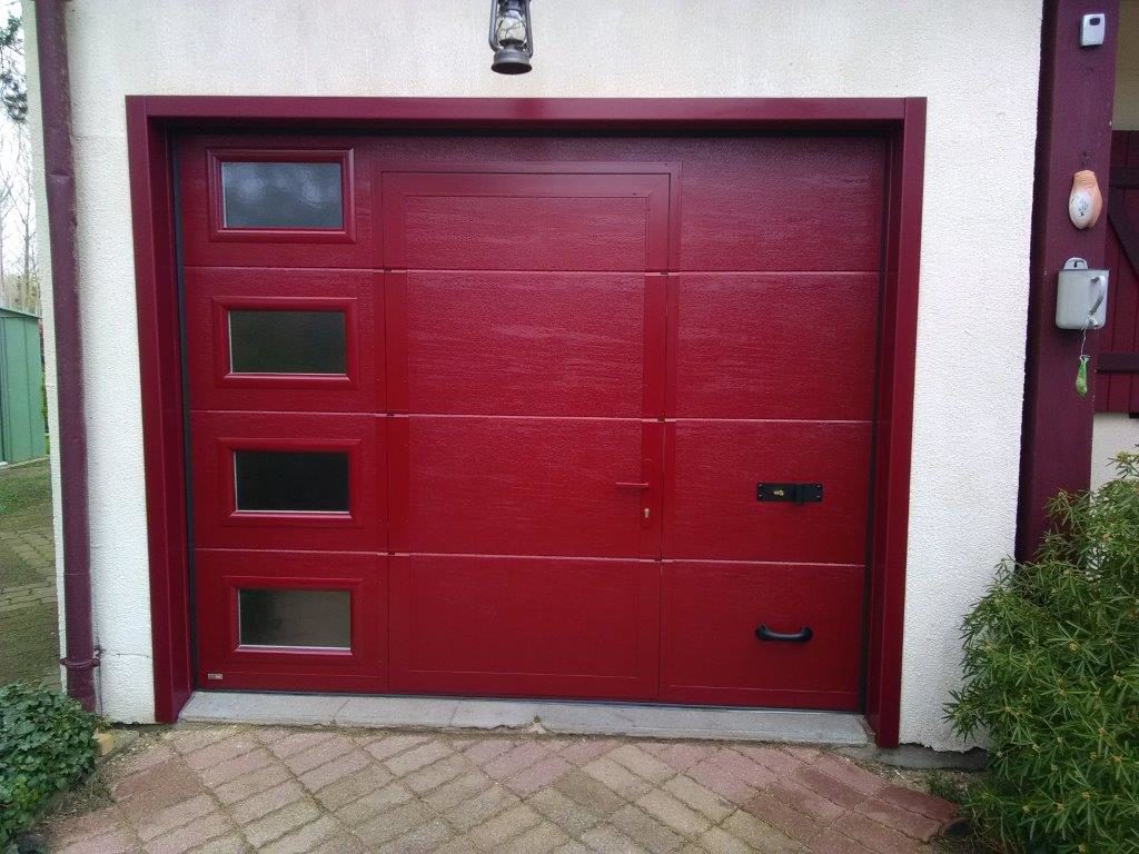 M2GB pose d'une porte de garage Sectionnelle rouge ral 3004 avec hublots et portillon intégré