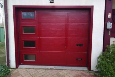 M2GB pose d'une porte de garage Sectionnelle rouge ral 3004 avec hublots et portillon intégré