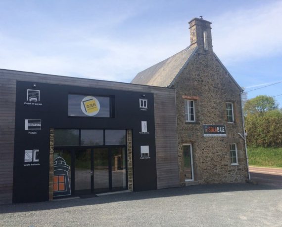 Devanture du magasin de votre installateur Solabaie OZEN Menuiserie, situé à Gratot dans la Manche. Pour vos projets en neuf ou rénovation de fenêtres, portes, volets et portails.