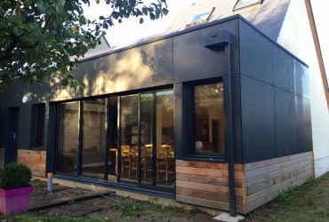 Extension d'habitation à ossature bois créée à Agneaux, disposant de menuiseries dont des baies coulissantes aluminium Solabaie, avec des volets roulants à motorisation Somfy