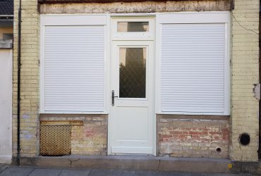 Porte d'entrée bois sur mesure modèle Persica avec imposte vitrée, accompagnée de volets roulants aluminium blanc intégrés sur les 2 fenêtres adjacentes. Réalisation effectuée par D'Eco Ouest